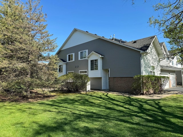 view of side of home with a lawn, roof with shingles, brick siding, and a garage
