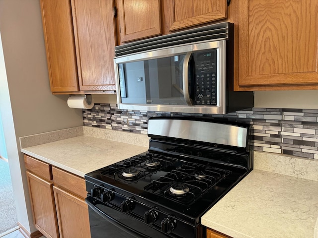 kitchen featuring stainless steel microwave, black gas range, decorative backsplash, and light countertops