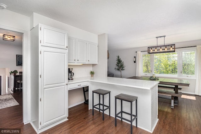 kitchen with dark wood-style floors, a peninsula, light countertops, white cabinetry, and a breakfast bar
