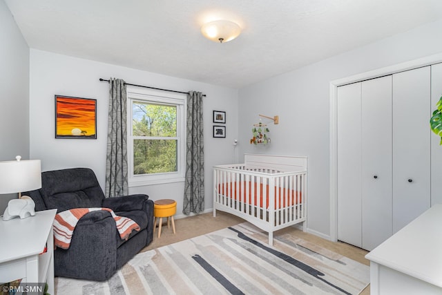 bedroom with light carpet, a closet, a crib, and baseboards