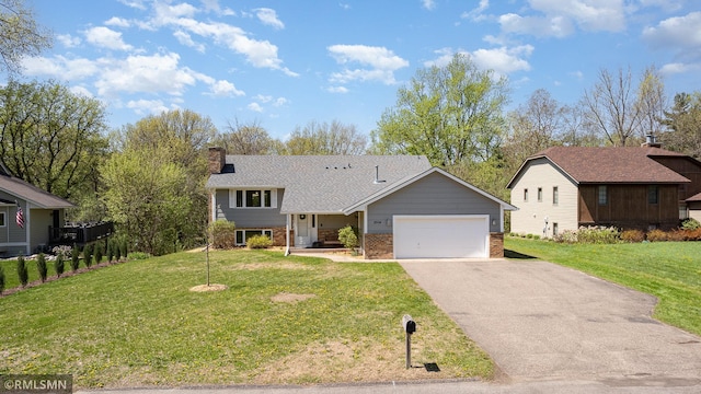 split level home featuring an attached garage, asphalt driveway, brick siding, a chimney, and a front lawn