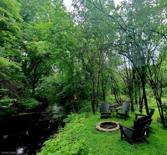 view of yard featuring an outdoor fire pit and a wooded view