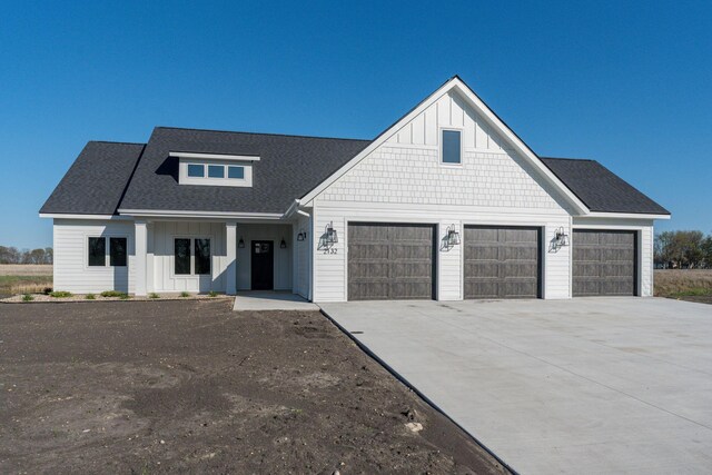 modern farmhouse with concrete driveway, board and batten siding, an attached garage, and roof with shingles