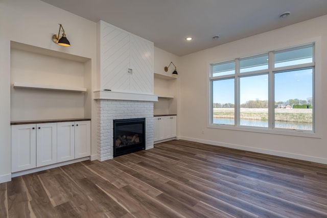 unfurnished living room featuring dark wood-type flooring, baseboards, a fireplace, built in features, and recessed lighting