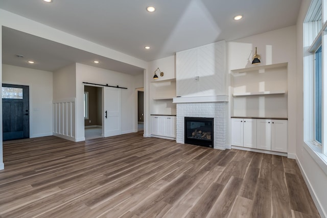 unfurnished living room with a barn door, wood finished floors, baseboards, a fireplace, and recessed lighting