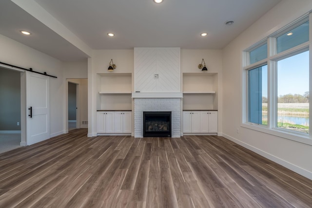 unfurnished living room featuring baseboards, plenty of natural light, dark wood-type flooring, a barn door, and recessed lighting
