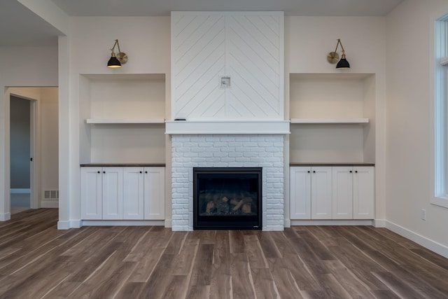 unfurnished living room featuring dark wood-style floors, built in shelves, baseboards, and a brick fireplace