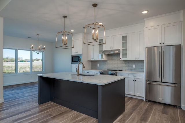 kitchen with a sink, under cabinet range hood, white cabinets, a notable chandelier, and appliances with stainless steel finishes