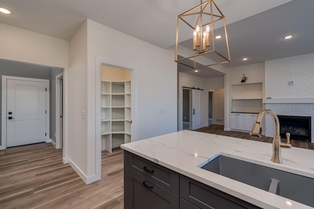 kitchen with a sink, wood finished floors, pendant lighting, light stone countertops, and recessed lighting