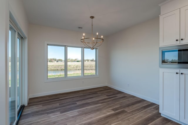 unfurnished dining area featuring a chandelier, dark wood-style floors, and baseboards