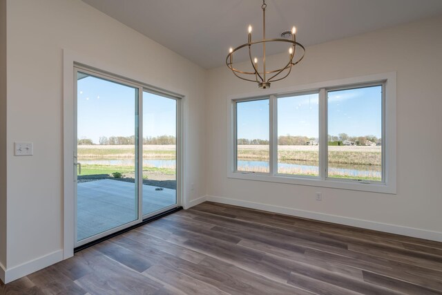 unfurnished dining area featuring a chandelier, baseboards, dark wood-type flooring, and a water view
