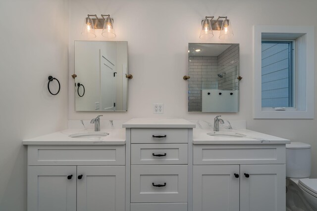 bathroom with toilet, two vanities, and tiled shower