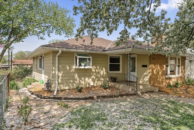 view of front of property with fence, roof with shingles, and brick siding