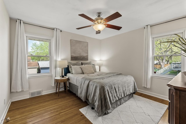bedroom featuring multiple windows, baseboards, wood finished floors, and a ceiling fan