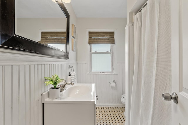 full bath with a wainscoted wall, toilet, and vanity