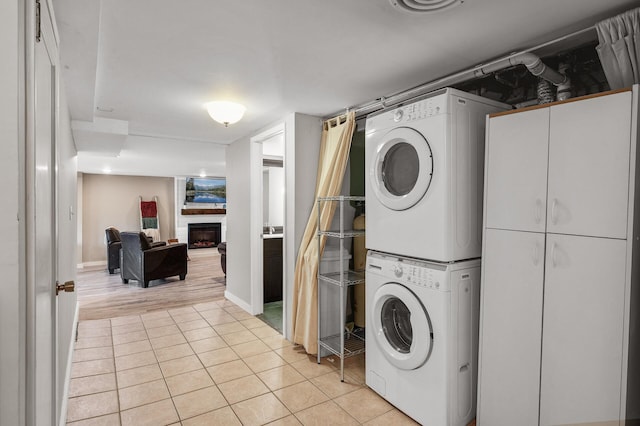 laundry room featuring stacked washer / dryer, a fireplace, and light tile patterned floors