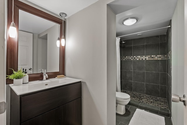 bathroom featuring toilet, tiled shower, vanity, and tile patterned flooring