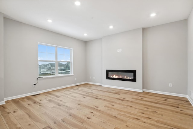 6746 Wildflower Way, Minnetrista, MN 55331 - unfurnished living room featuring light wood finished floors, recessed lighting, a glass covered fireplace, and baseboards