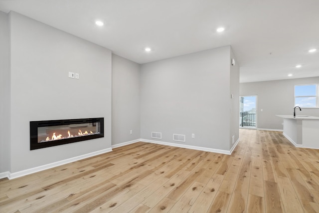 6746 Wildflower Way, Minnetrista, MN 55331 - unfurnished living room featuring light wood-type flooring, a glass covered fireplace, recessed lighting, a sink, and baseboards