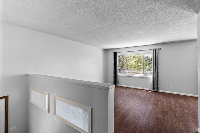 unfurnished room featuring dark wood finished floors, a textured ceiling, and baseboards