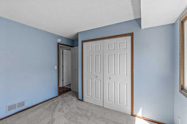 unfurnished bedroom featuring light carpet, a closet, a textured ceiling, and baseboards
