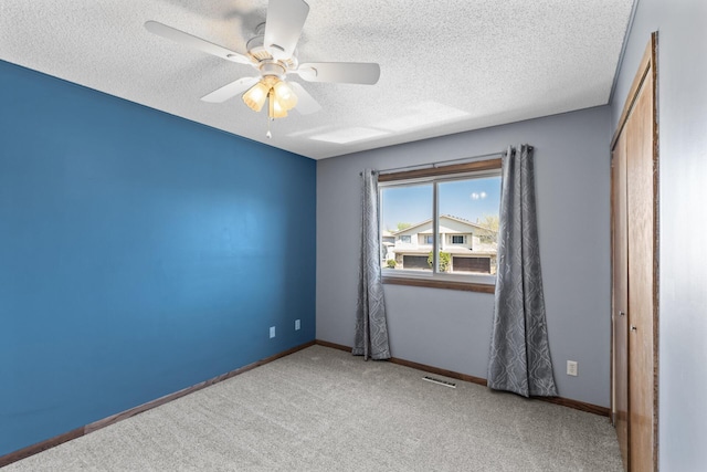 spare room with a textured ceiling, carpet flooring, ceiling fan, and baseboards