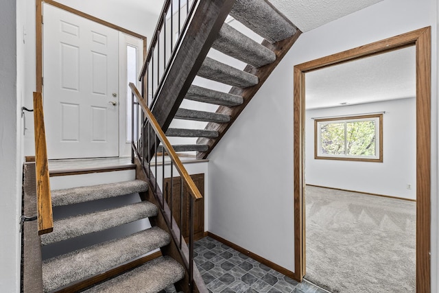 stairway featuring a textured ceiling, baseboards, and carpet