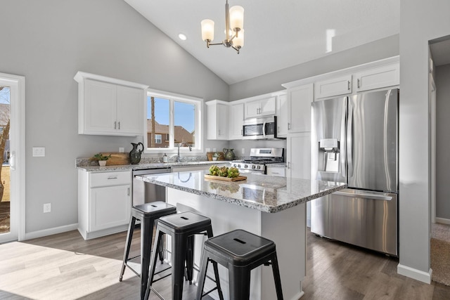 kitchen featuring light stone counters, white cabinets, appliances with stainless steel finishes, and high vaulted ceiling