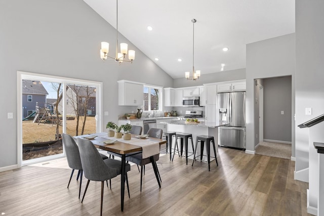 dining area with a chandelier, baseboards, high vaulted ceiling, and wood finished floors
