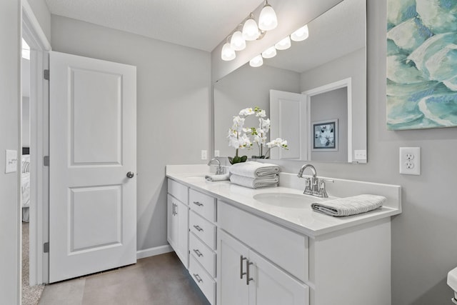 ensuite bathroom with double vanity, connected bathroom, baseboards, and a sink