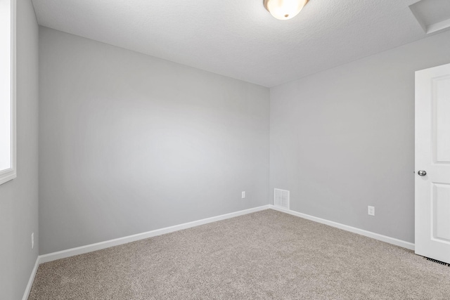 carpeted empty room with a textured ceiling, attic access, baseboards, and visible vents