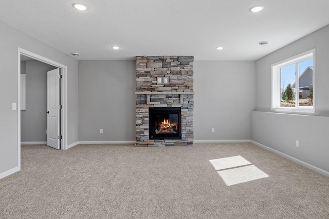 unfurnished living room with baseboards, a stone fireplace, recessed lighting, and carpet