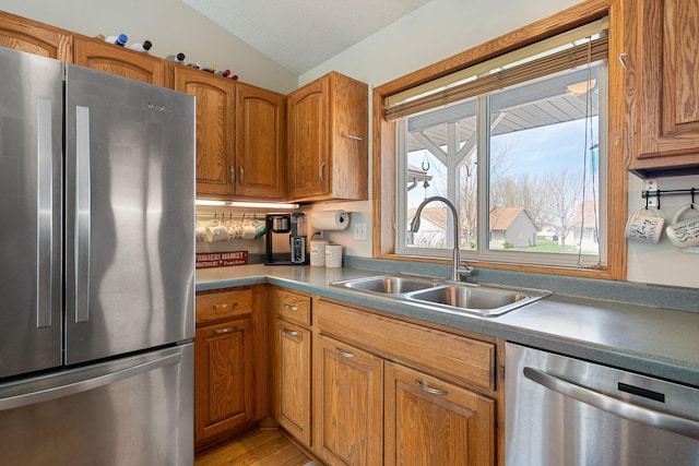 404 6th St NW, New Richland, MN 56072 - kitchen featuring appliances with stainless steel finishes, a sink, vaulted ceiling, brown cabinetry, and light wood-style floors
