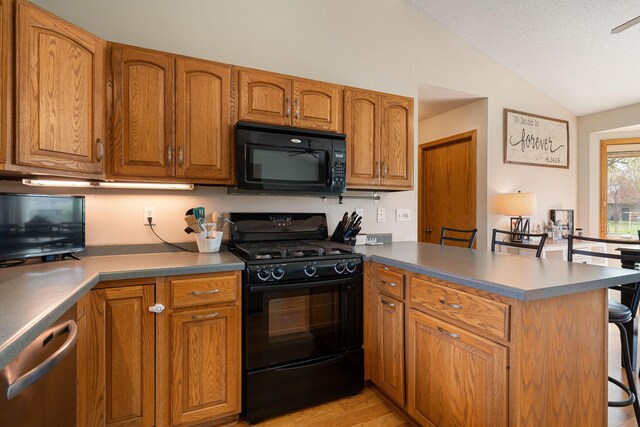 404 6th St NW, New Richland, MN 56072 - kitchen with black appliances, a peninsula, lofted ceiling, brown cabinetry, and a breakfast bar