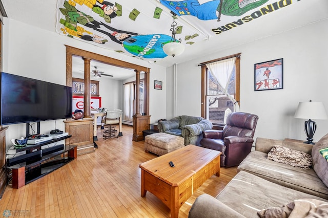 living area featuring light wood finished floors, a baseboard radiator, and ornate columns