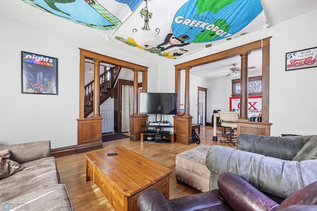 living area featuring baseboards, radiator, decorative columns, wood finished floors, and stairway
