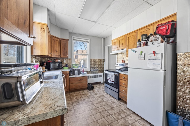 kitchen featuring freestanding refrigerator, under cabinet range hood, tasteful backsplash, and stainless steel electric stove