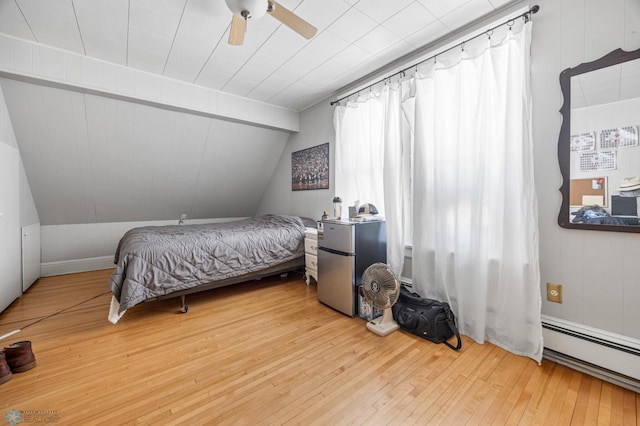 bedroom with lofted ceiling, hardwood / wood-style floors, freestanding refrigerator, a ceiling fan, and baseboard heating