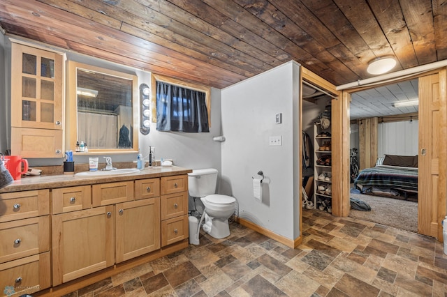 bathroom with toilet, vanity, stone finish flooring, wood ceiling, and baseboards