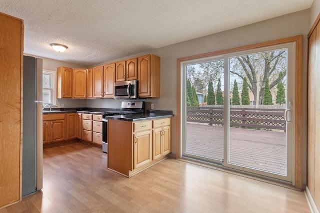 kitchen with stainless steel appliances, light wood-style floors, a textured ceiling, dark countertops, and a sink