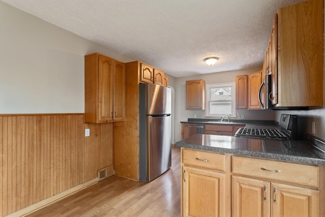 kitchen with stainless steel appliances, light wood-style floors, dark countertops, a textured ceiling, and a peninsula