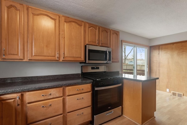 kitchen with stainless steel appliances, dark countertops, a textured ceiling, and light wood-style flooring