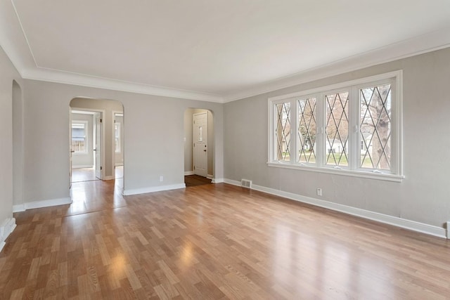 empty room featuring arched walkways, wood finished floors, ornamental molding, and baseboards