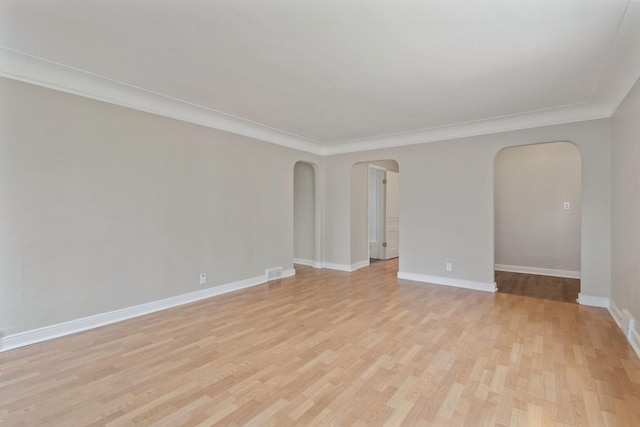 empty room with arched walkways, light wood-style floors, baseboards, and crown molding