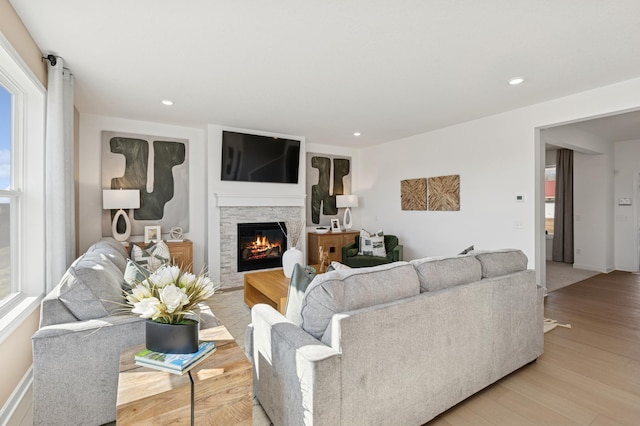 living area with recessed lighting, a stone fireplace, and light wood-style floors