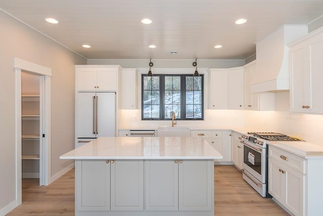 kitchen featuring range with gas stovetop, white built in fridge, a sink, a center island, and white cabinets