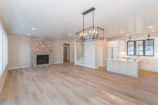 unfurnished living room with light wood-style flooring, a chandelier, recessed lighting, a stone fireplace, and baseboards