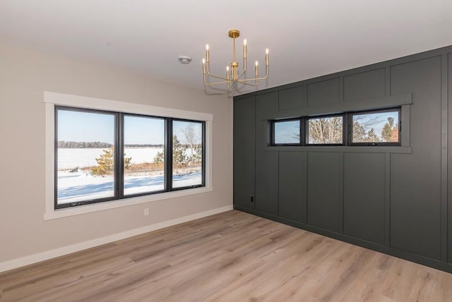 spare room with a chandelier, plenty of natural light, light wood-style flooring, and baseboards