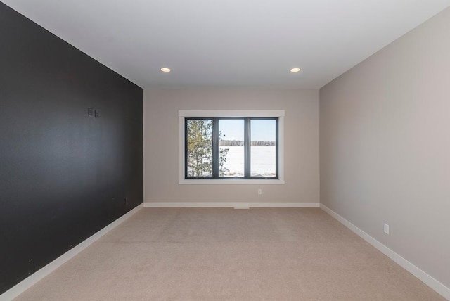 spare room with recessed lighting, light carpet, baseboards, and a water view
