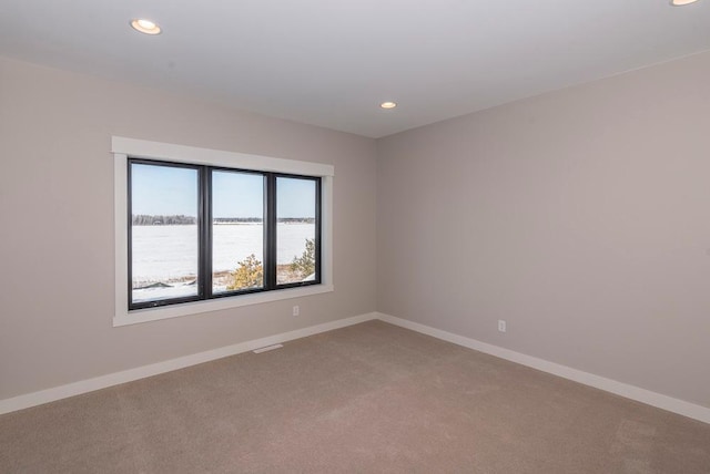 empty room with a water view, recessed lighting, light colored carpet, and baseboards